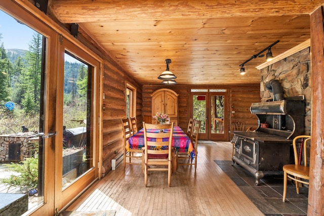 dining space featuring track lighting, hardwood / wood-style flooring, a wood stove, and log walls