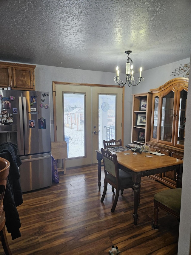 dining area with dark wood-type flooring, a textured ceiling, and an inviting chandelier