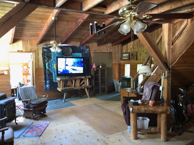 living area with ceiling fan, lofted ceiling with beams, a wood stove, wood walls, and wood ceiling