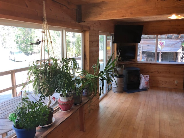 interior space featuring beamed ceiling, wood walls, light wood-style flooring, and a wood stove