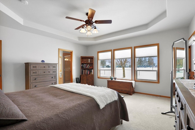 bedroom with light carpet, a raised ceiling, a ceiling fan, baseboards, and ensuite bathroom