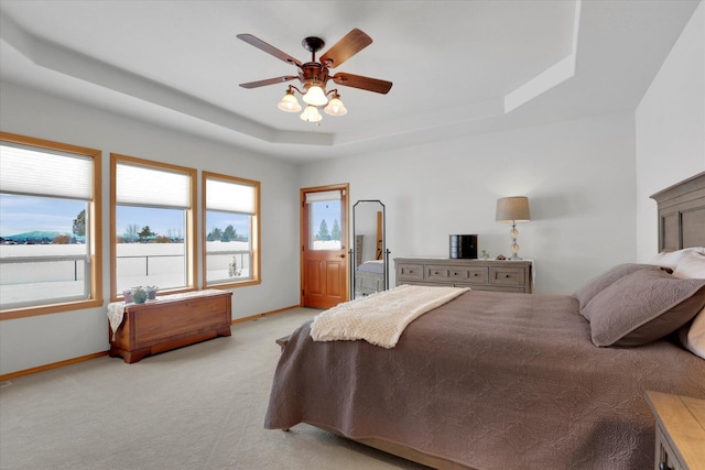 bedroom featuring a raised ceiling, baseboards, light carpet, and a ceiling fan