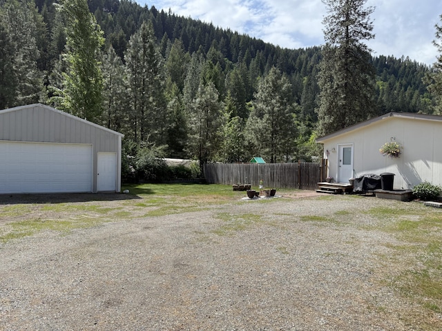 view of yard with a forest view, fence, an outdoor structure, and a garage