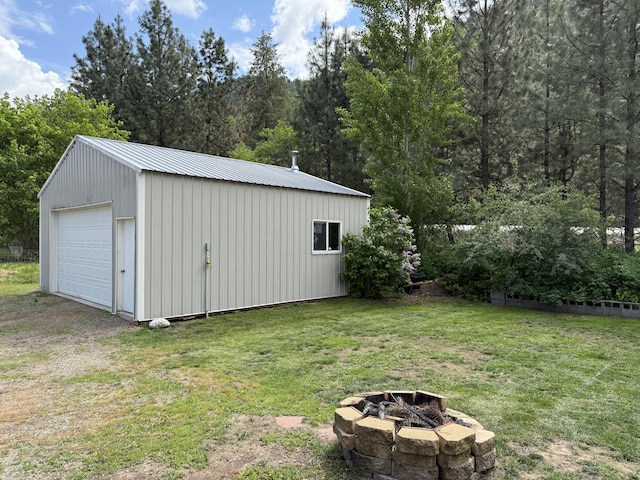 view of grassy yard featuring an outdoor fire pit, a detached garage, and an outbuilding