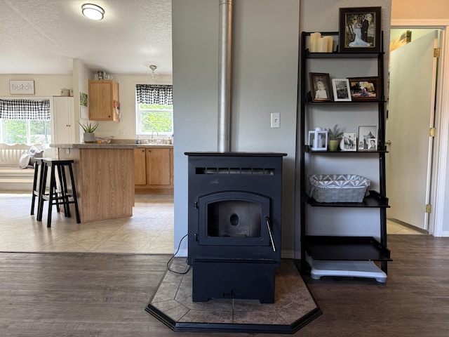 kitchen with a wood stove, a breakfast bar, light wood finished floors, light brown cabinets, and a textured ceiling