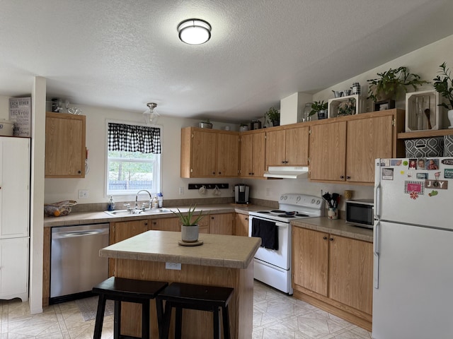 kitchen featuring stainless steel appliances, a sink, under cabinet range hood, a textured ceiling, and a center island