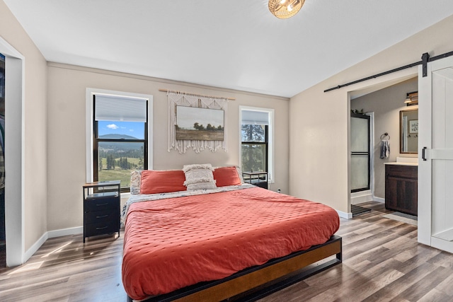 bedroom featuring lofted ceiling, a barn door, baseboards, light wood finished floors, and ensuite bath