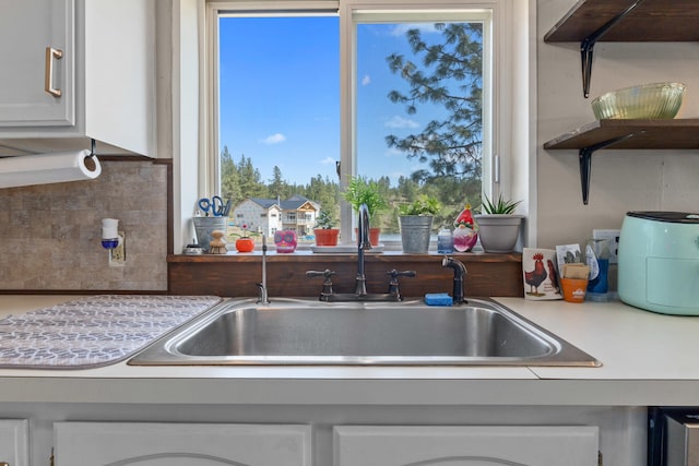 kitchen with backsplash, a wealth of natural light, light countertops, and a sink