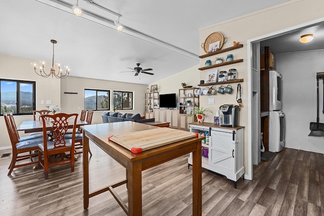 rec room with ceiling fan with notable chandelier, stacked washer and clothes dryer, a wealth of natural light, and dark wood-style flooring