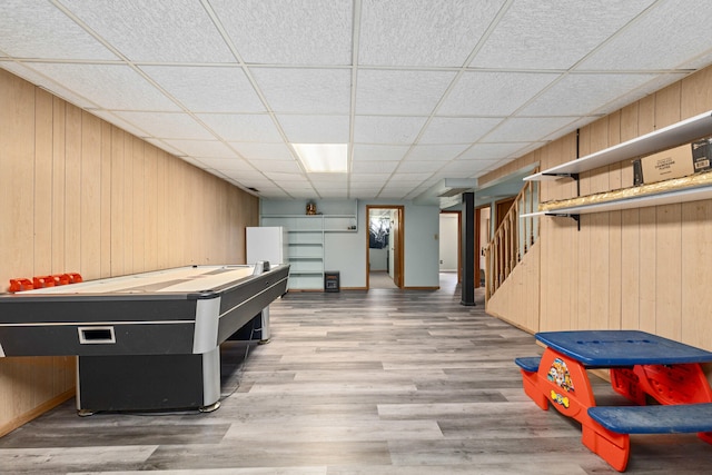 rec room featuring wood finished floors, wooden walls, and a drop ceiling