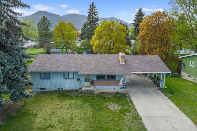 view of front of home with a chimney, a carport, a mountain view, a front lawn, and concrete driveway