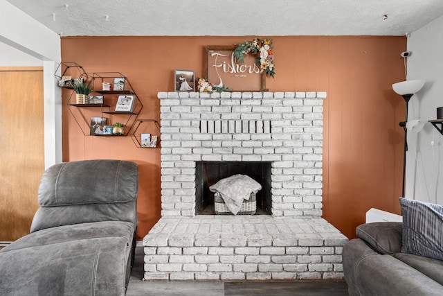 living area with a brick fireplace, a textured ceiling, and wood finished floors