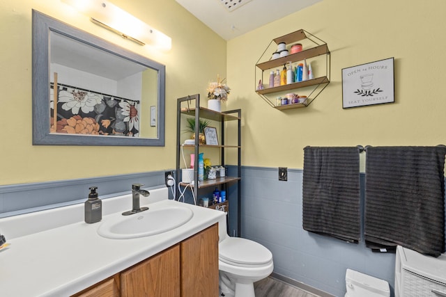 bathroom with toilet, tile walls, wood finished floors, vanity, and wainscoting
