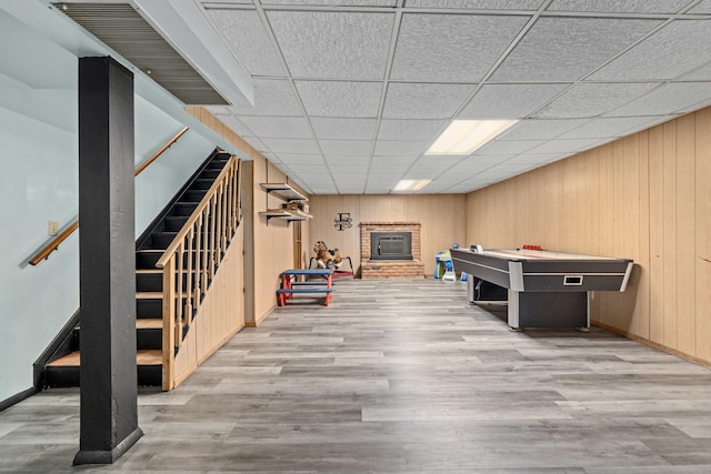 game room with wooden walls, a brick fireplace, wood finished floors, and baseboards