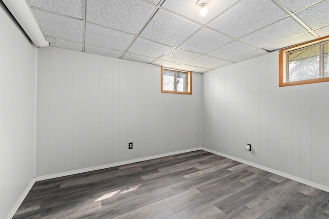 below grade area with baseboards, wood finished floors, and a drop ceiling