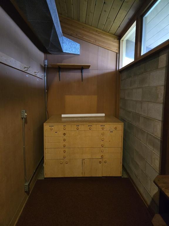 basement featuring dark carpet, concrete block wall, and wooden ceiling