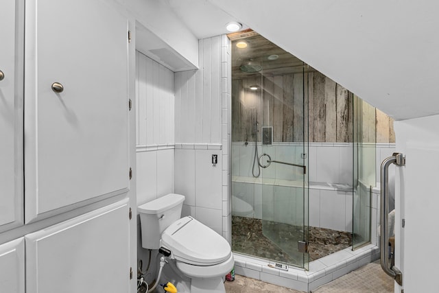 bathroom featuring tile patterned floors, toilet, walk in shower, and tile walls