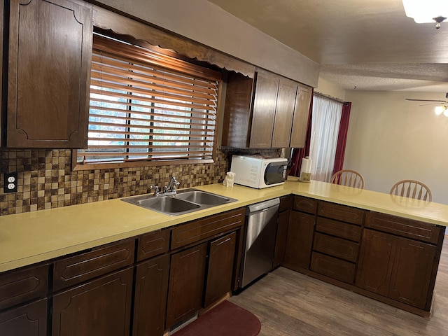 kitchen with kitchen peninsula, stainless steel dishwasher, ceiling fan, sink, and tasteful backsplash