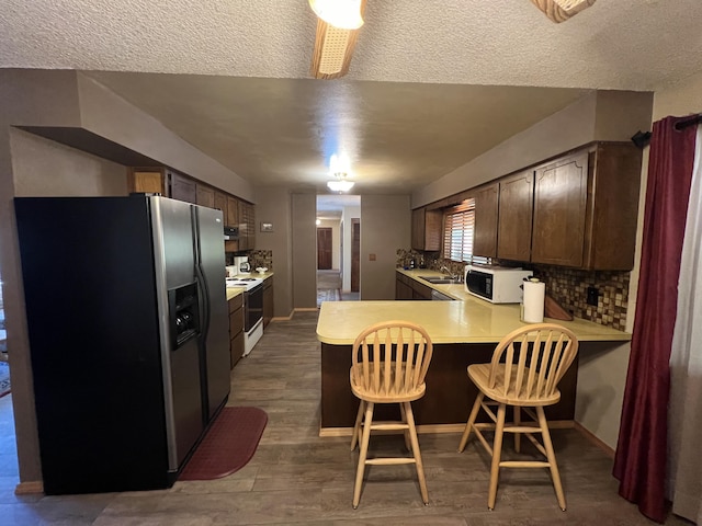 kitchen with white appliances, a kitchen breakfast bar, sink, kitchen peninsula, and backsplash