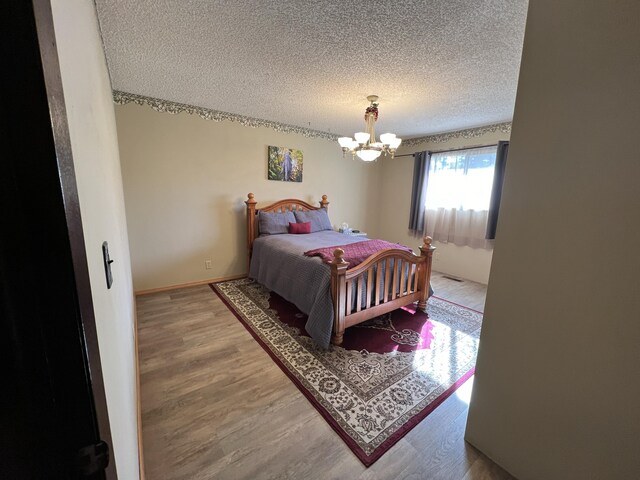 bedroom with hardwood / wood-style flooring, ceiling fan with notable chandelier, and a textured ceiling