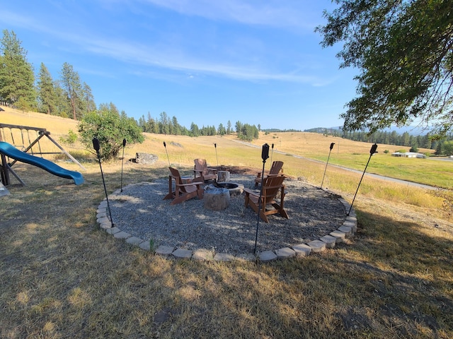 view of yard featuring a rural view, a playground, and a fire pit