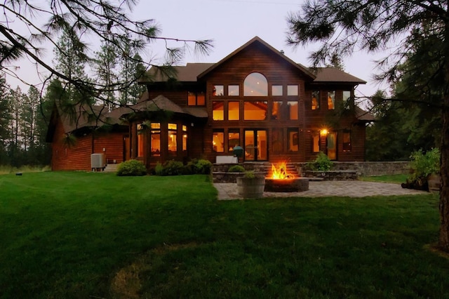 back house at dusk with a patio, an outdoor fire pit, a lawn, and central air condition unit