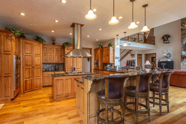 kitchen featuring kitchen peninsula, decorative light fixtures, tasteful backsplash, a kitchen bar, and island range hood