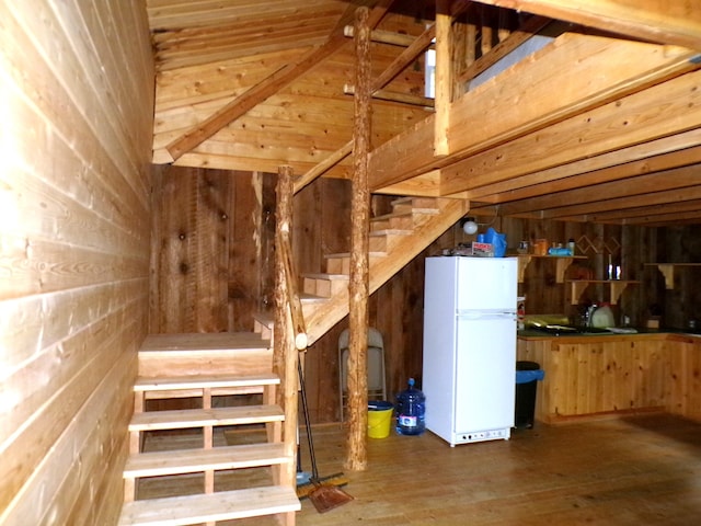 basement with white refrigerator, dark wood-type flooring, and wooden walls