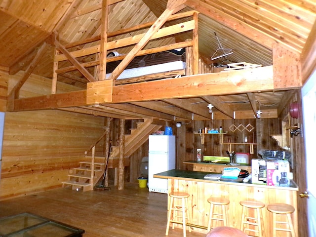 kitchen featuring wood finished floors, high vaulted ceiling, a peninsula, freestanding refrigerator, and wood walls