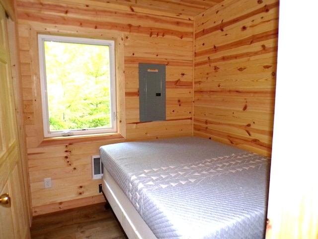 bedroom featuring electric panel, visible vents, wooden walls, and wood finished floors