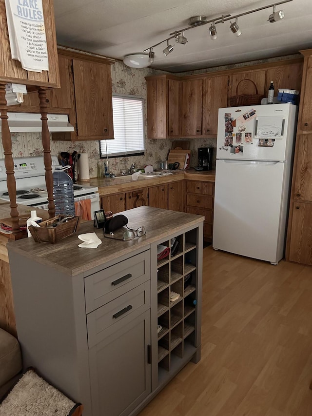 2952 Deep Lake Boundary Rd, Colville, WA 99114 - kitchen with white appliances, under cabinet range hood, light wood-type flooring, brown cabinets, and backsplash