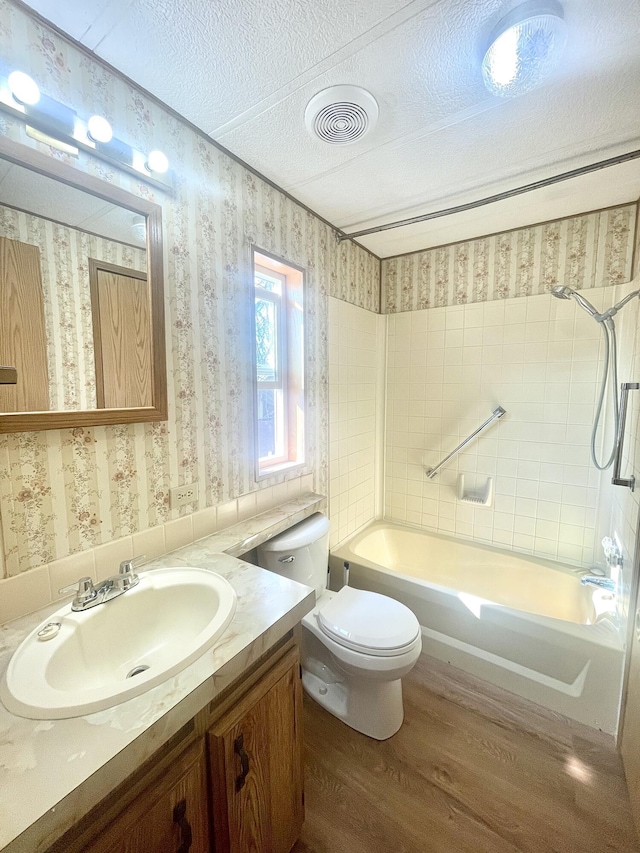 full bathroom with a textured ceiling, tiled shower / bath, wood-type flooring, vanity, and toilet