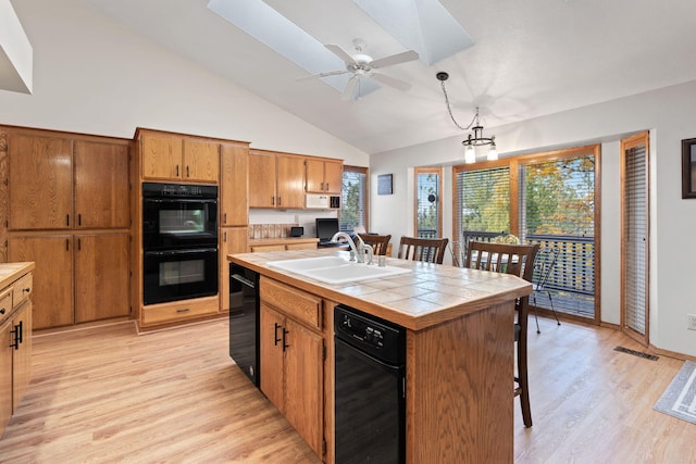 4203 S Suncrest Ln, Spokane Valley, WA 99037 - kitchen with black appliances, tile counters, light wood-type flooring, brown cabinets, and a breakfast bar area