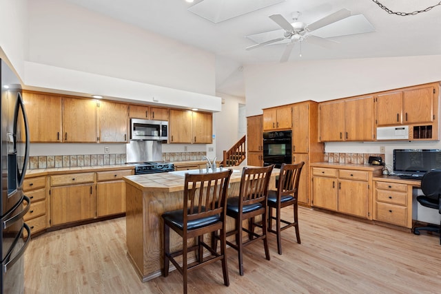 4203 S Suncrest Ln, Spokane Valley, WA 99037 - kitchen with black appliances, light wood-style flooring, tile countertops, a ceiling fan, and a kitchen bar