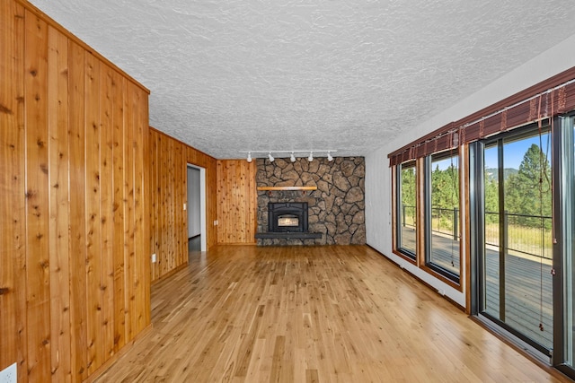 unfurnished living room with a textured ceiling, a stone fireplace, light hardwood / wood-style floors, rail lighting, and wood walls