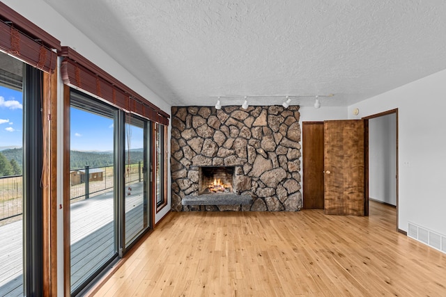 unfurnished living room featuring a stone fireplace, light wood-type flooring, a textured ceiling, and track lighting