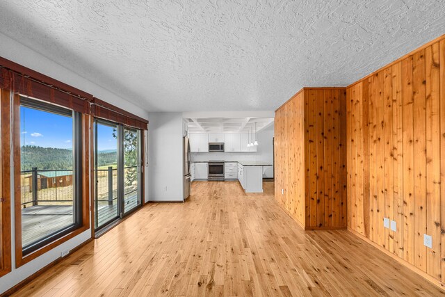 unfurnished living room with wood walls, light hardwood / wood-style floors, and a textured ceiling