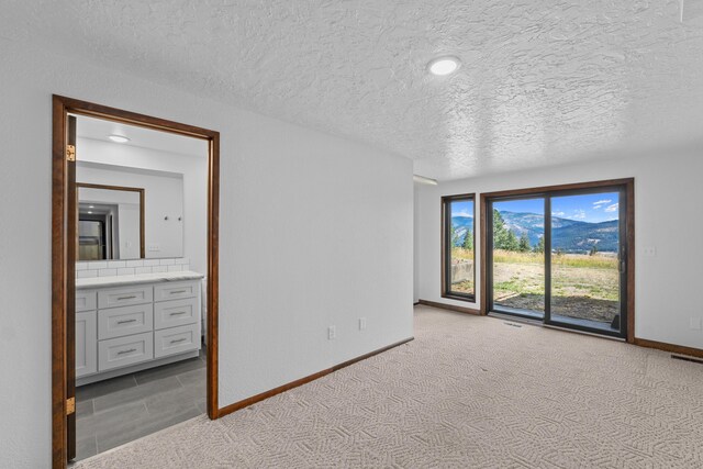 interior space with a textured ceiling, access to exterior, light colored carpet, and ensuite bath