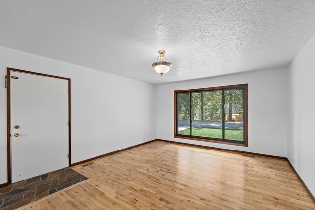 unfurnished room with light wood-type flooring and a textured ceiling