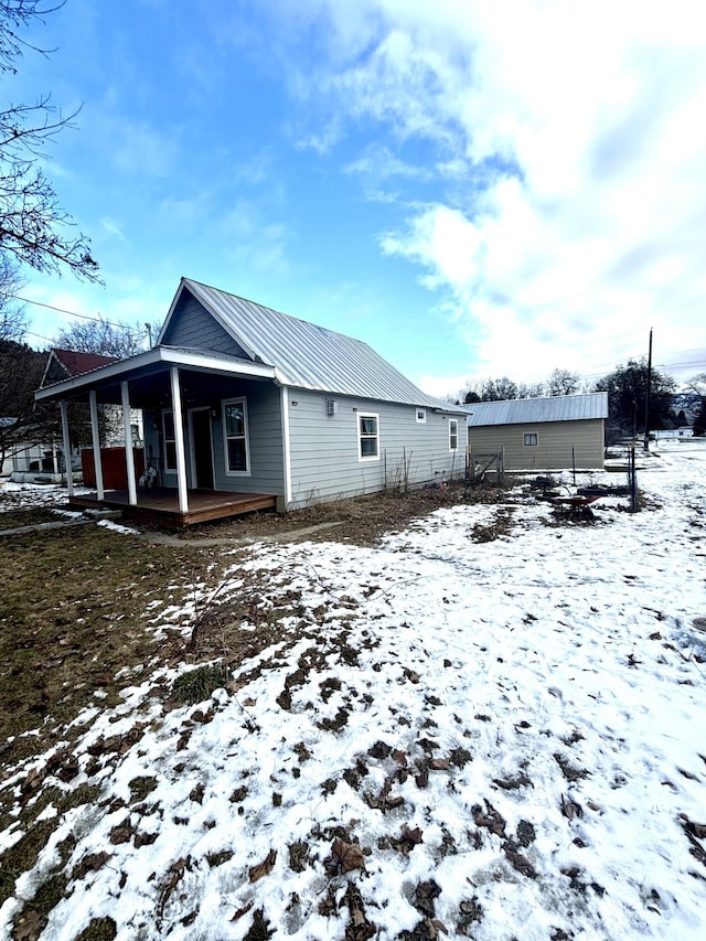 snow covered rear of property with covered porch and metal roof