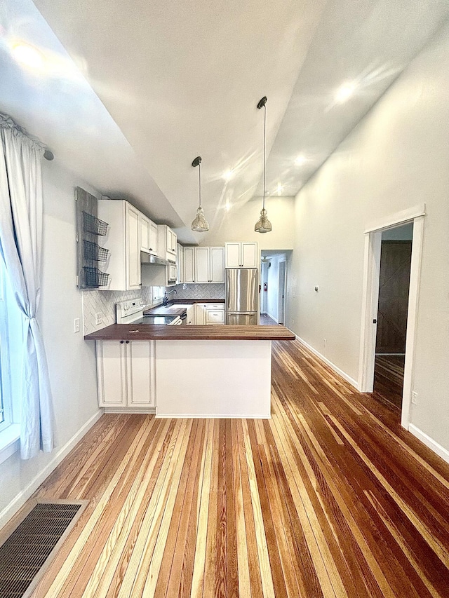 kitchen with dark countertops, visible vents, freestanding refrigerator, white cabinetry, and a peninsula