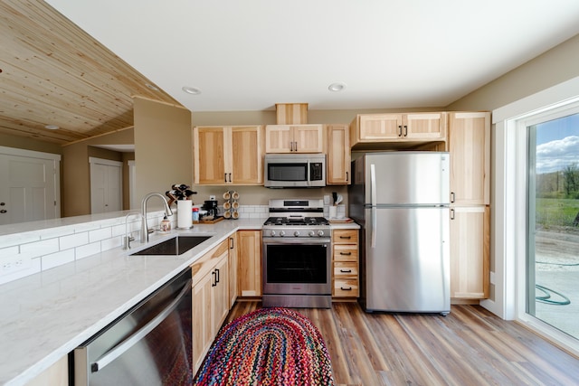 kitchen featuring light brown cabinets, a sink, vaulted ceiling, appliances with stainless steel finishes, and light wood-type flooring