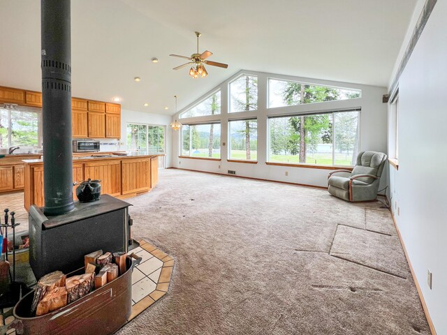 carpeted living room featuring high vaulted ceiling, a wood stove, and ceiling fan