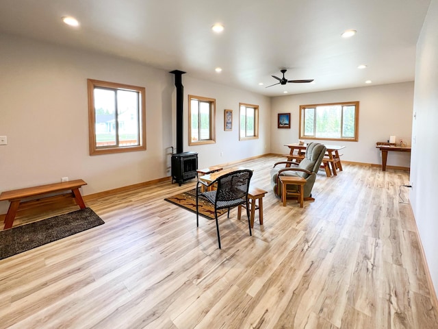 living room with ceiling fan, a wood stove, and light wood-type flooring