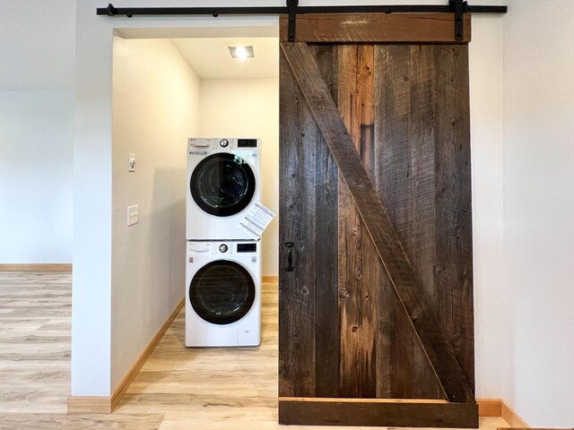 clothes washing area with light hardwood / wood-style floors, stacked washer and clothes dryer, and a barn door