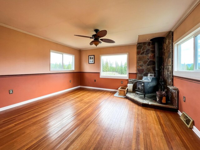 unfurnished living room with ceiling fan, hardwood / wood-style flooring, a wood stove, and ornamental molding