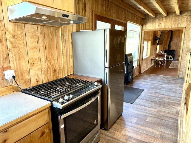 3305 Bradeen Rd, Rice, WA 99167 - kitchen featuring stainless steel appliances, under cabinet range hood, wood walls, light wood-type flooring, and a wood stove