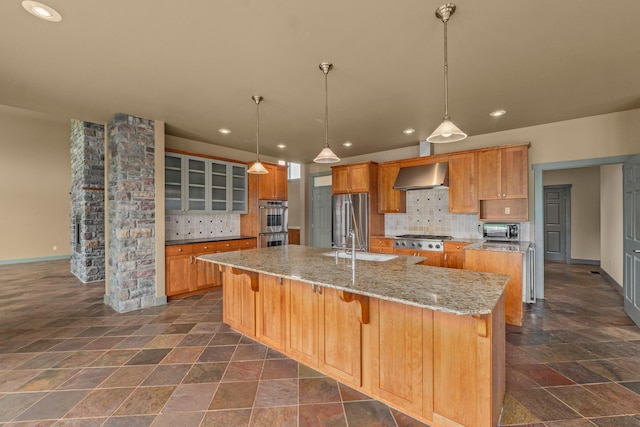 kitchen with tasteful backsplash, a large island with sink, hanging light fixtures, stainless steel appliances, and wall chimney range hood