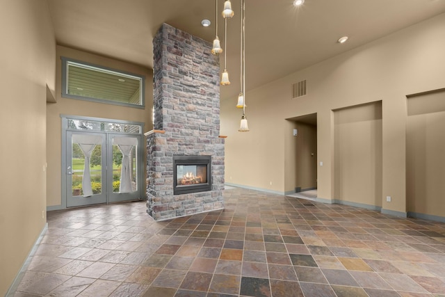 unfurnished living room featuring a stone fireplace, french doors, and a high ceiling