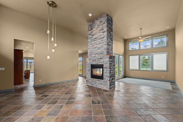 unfurnished living room with a stone fireplace, ceiling fan, and a high ceiling